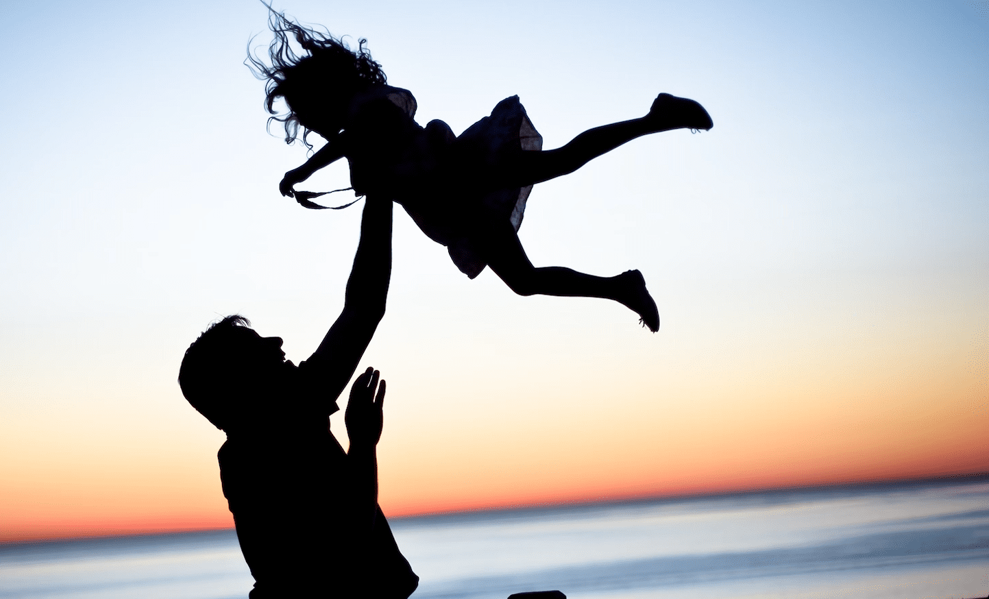 Father throwing his daughter in the air at sunset.